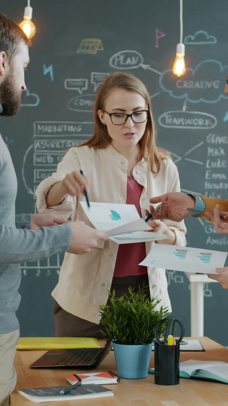 A marketing team planning a campaign together at a table, in front of a chalkboard mapping out marketing, advertising, web and teamwork