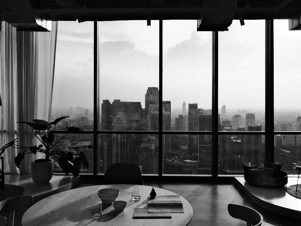 A calm, modern office with floor-to-ceiling windows overlooking a city skyline, in black and white